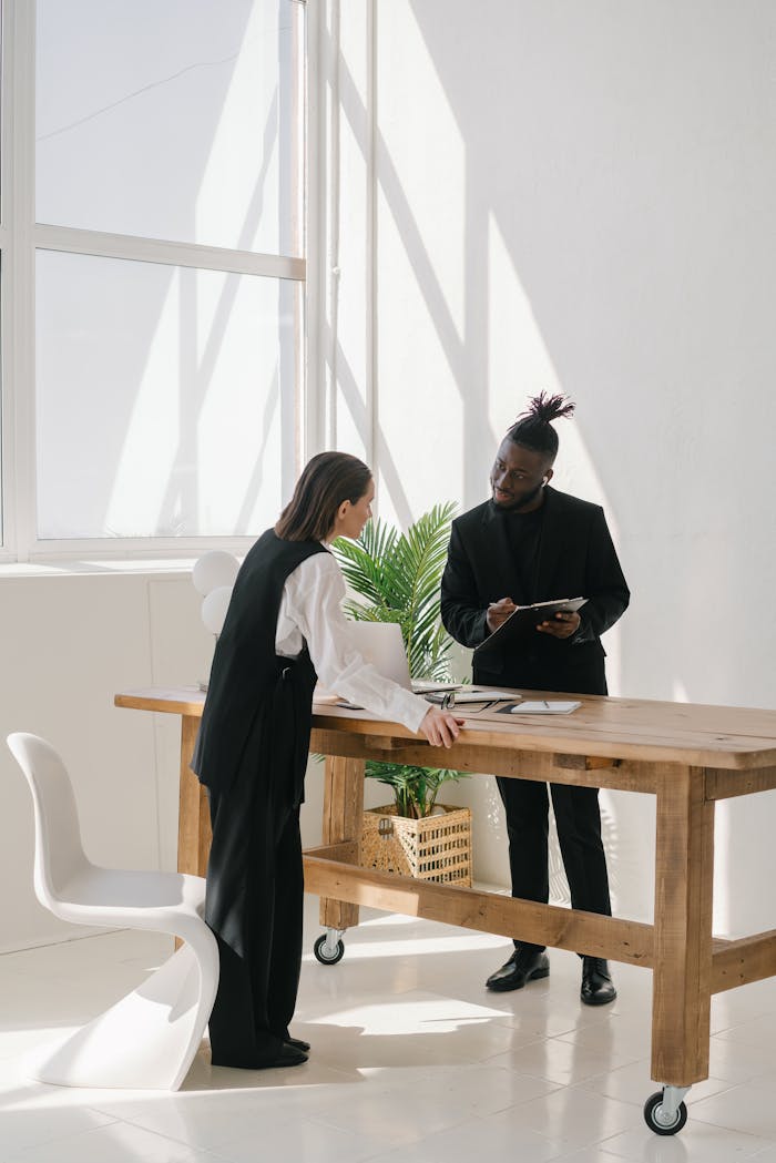 Two professionals engaged in a meeting at a wooden table in a bright, modern office.